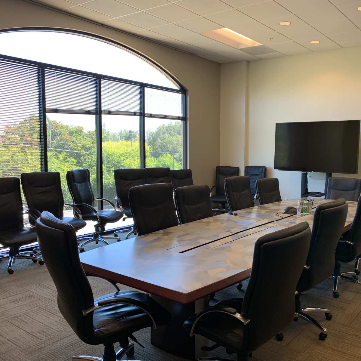A large conference room with a long table surrounded by black chairs, a television mounted on the wall, and a whiteboard.