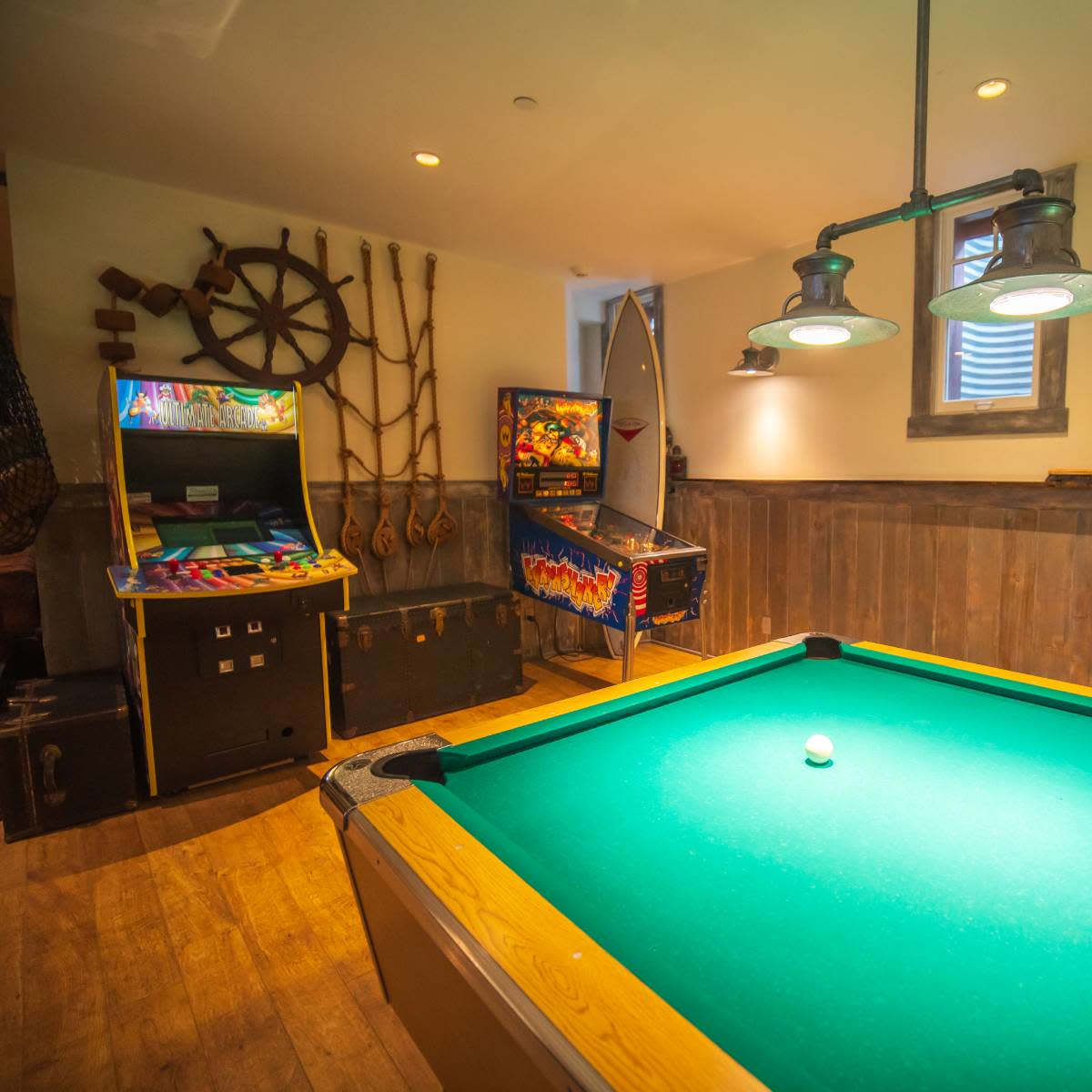 A game room featuring a pool table, arcade machines, and wall-mounted pegboards with sports equipment.