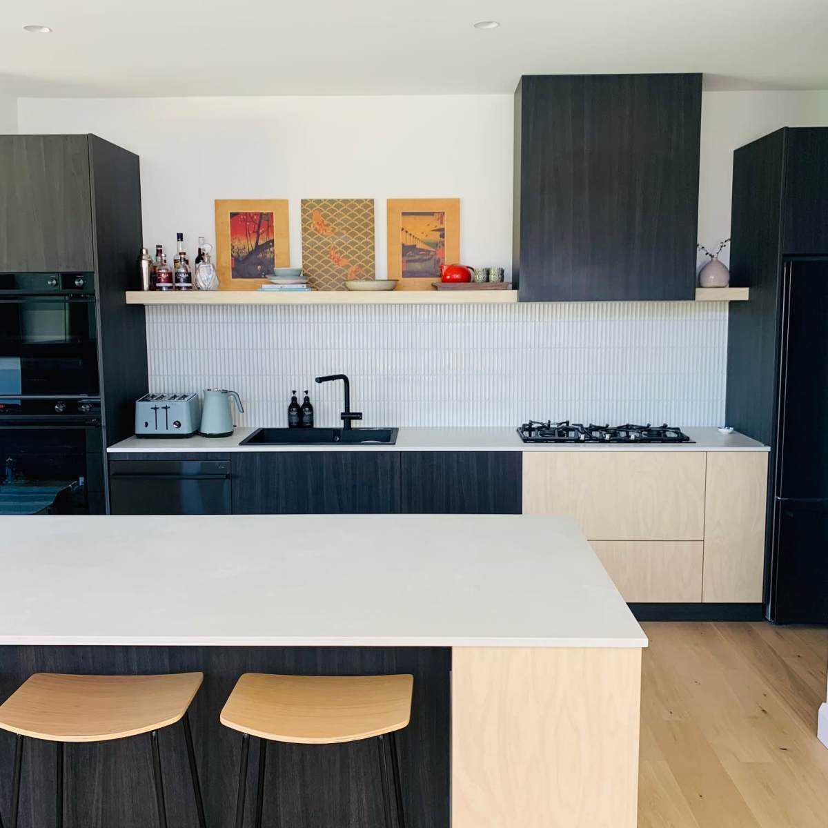 A modern kitchen features dark cabinetry, a light-colored countertop, and two wooden bar stools at an island.