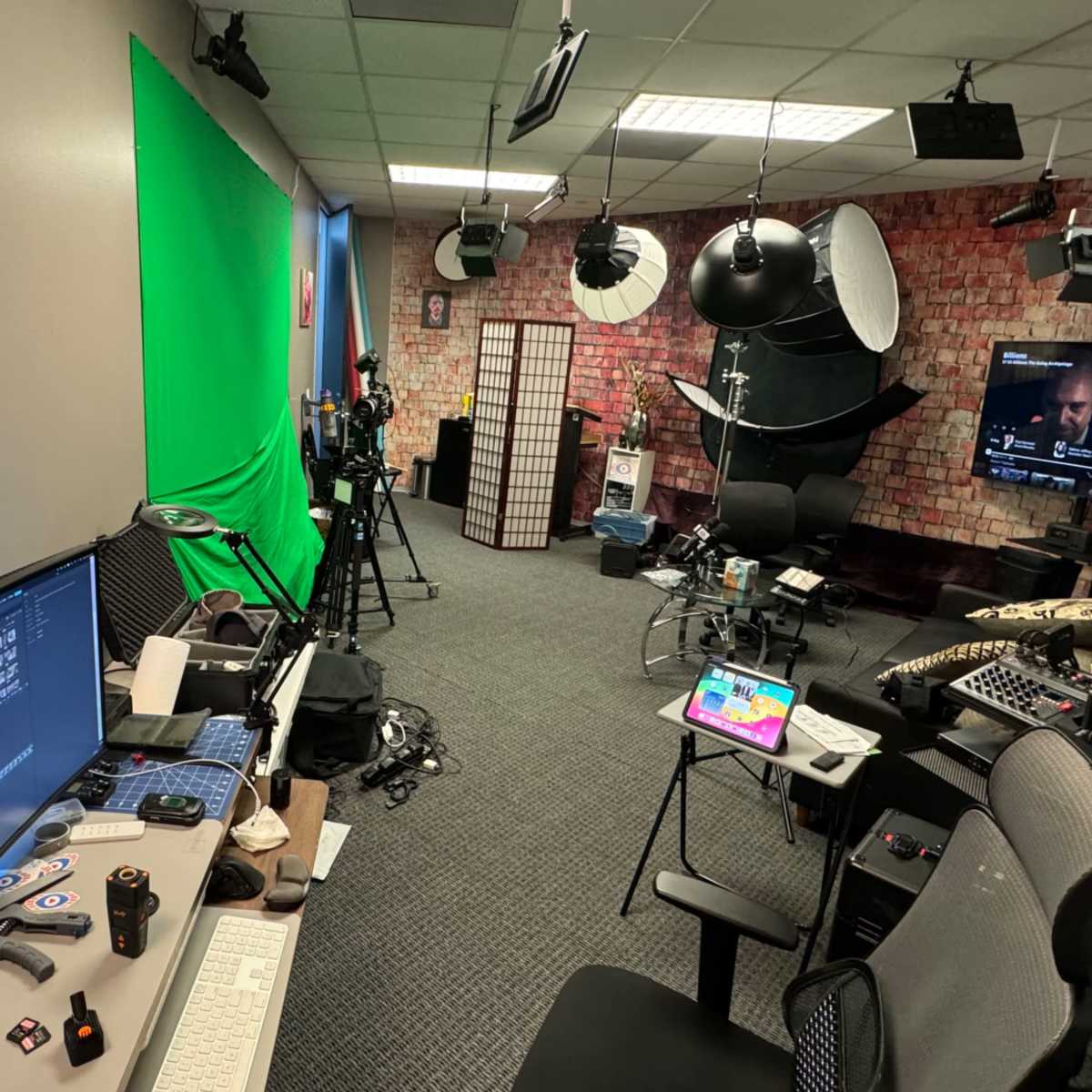 A recording studio equipped with a green screen, cameras, lighting equipment, and computer workstations.