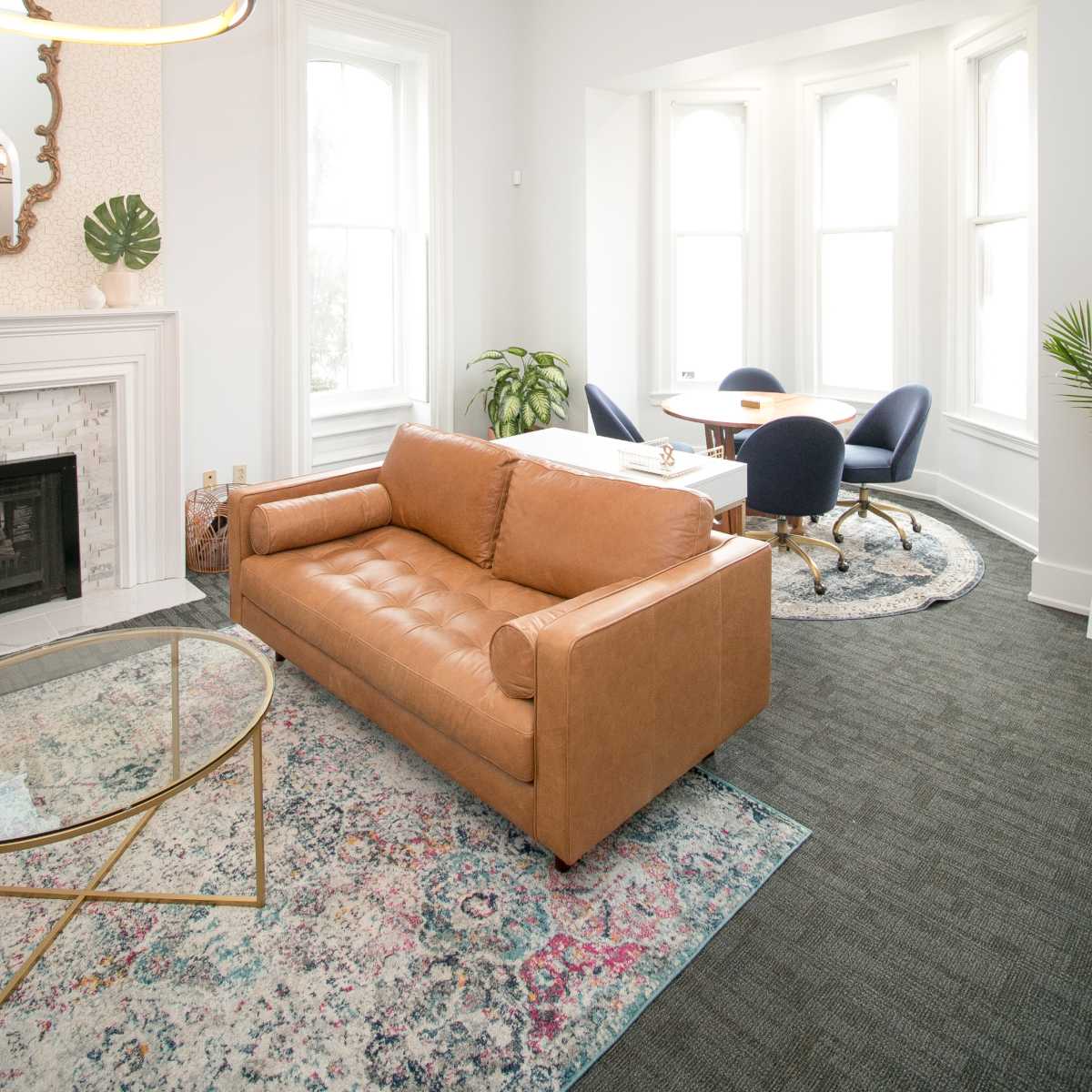 A modern living area with a brown leather sofa, a round coffee table, and a corner with large windows.