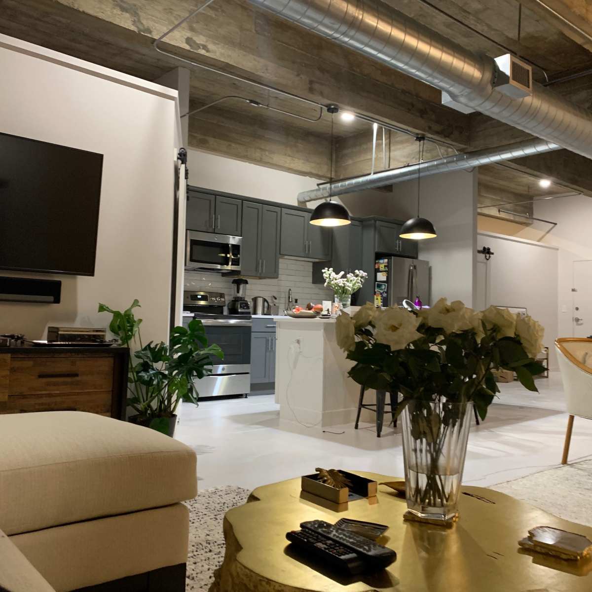 A modern, open-concept living space featuring a comfortable couch, a television mounted on the wall, a kitchen in the background, and a dining area with a decorative table.