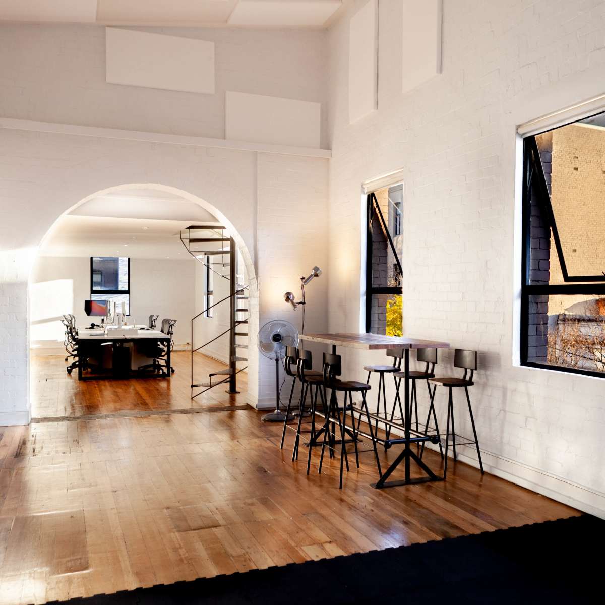 A bright, open studio space featuring wooden floors, a bar-style seating area, and a spiral staircase leading to an upper level.