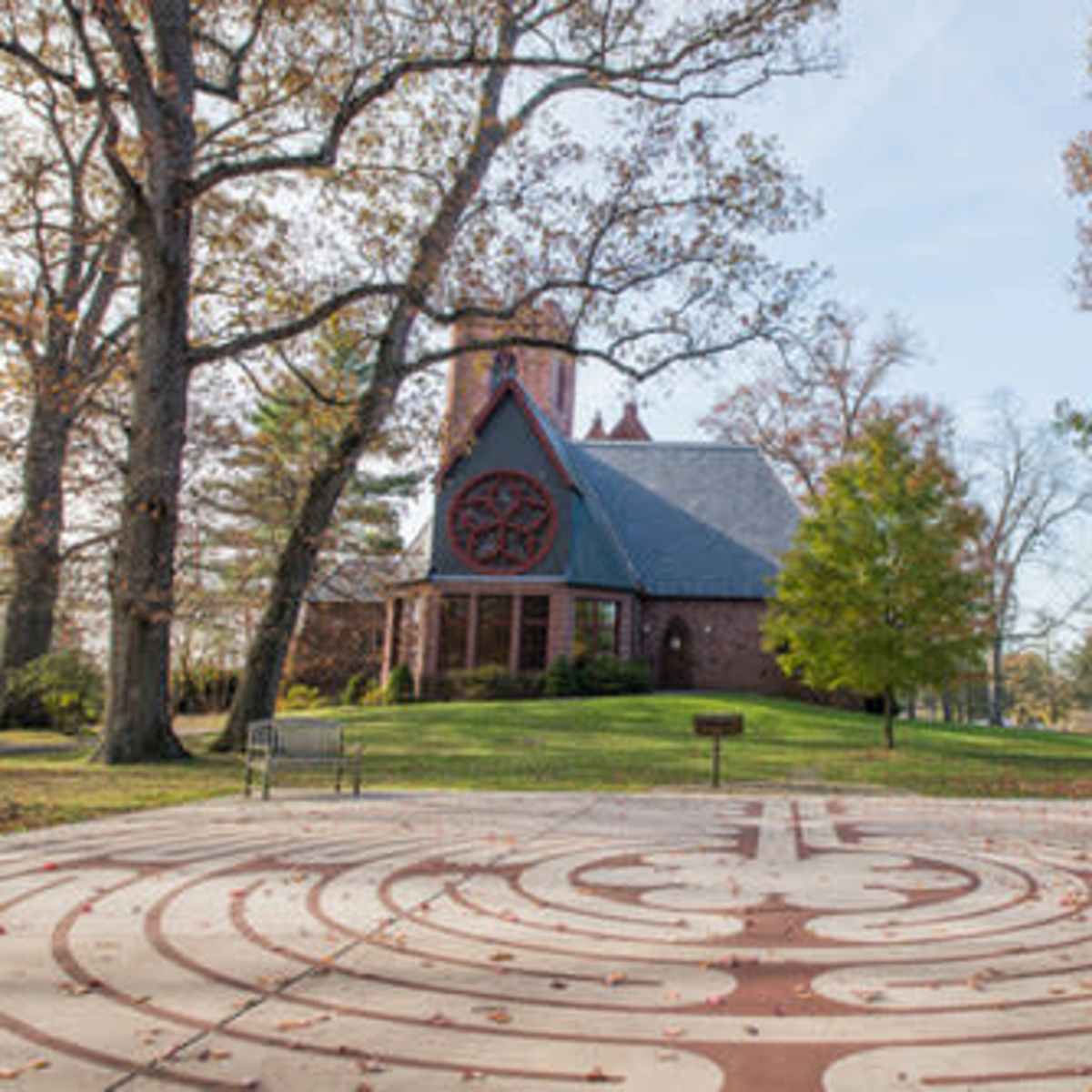 A stone labyrinth is set in a park in front of a brick church surrounded by trees.