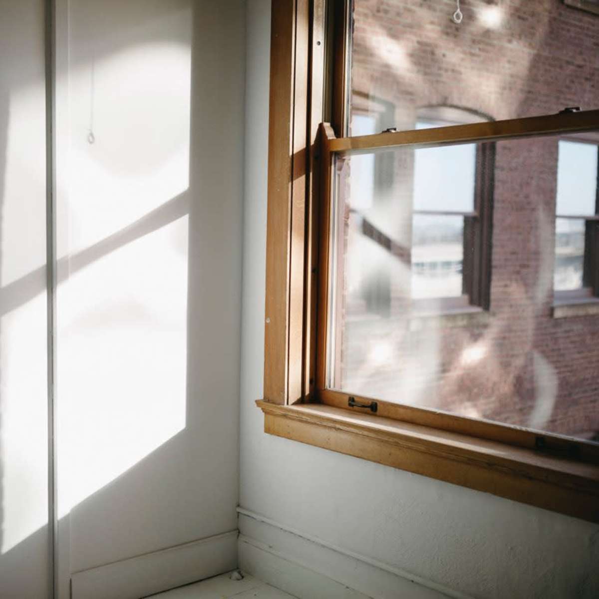 A sunlight-drenched corner of a room features a window with wooden trim and a shadow cast on the wall.
