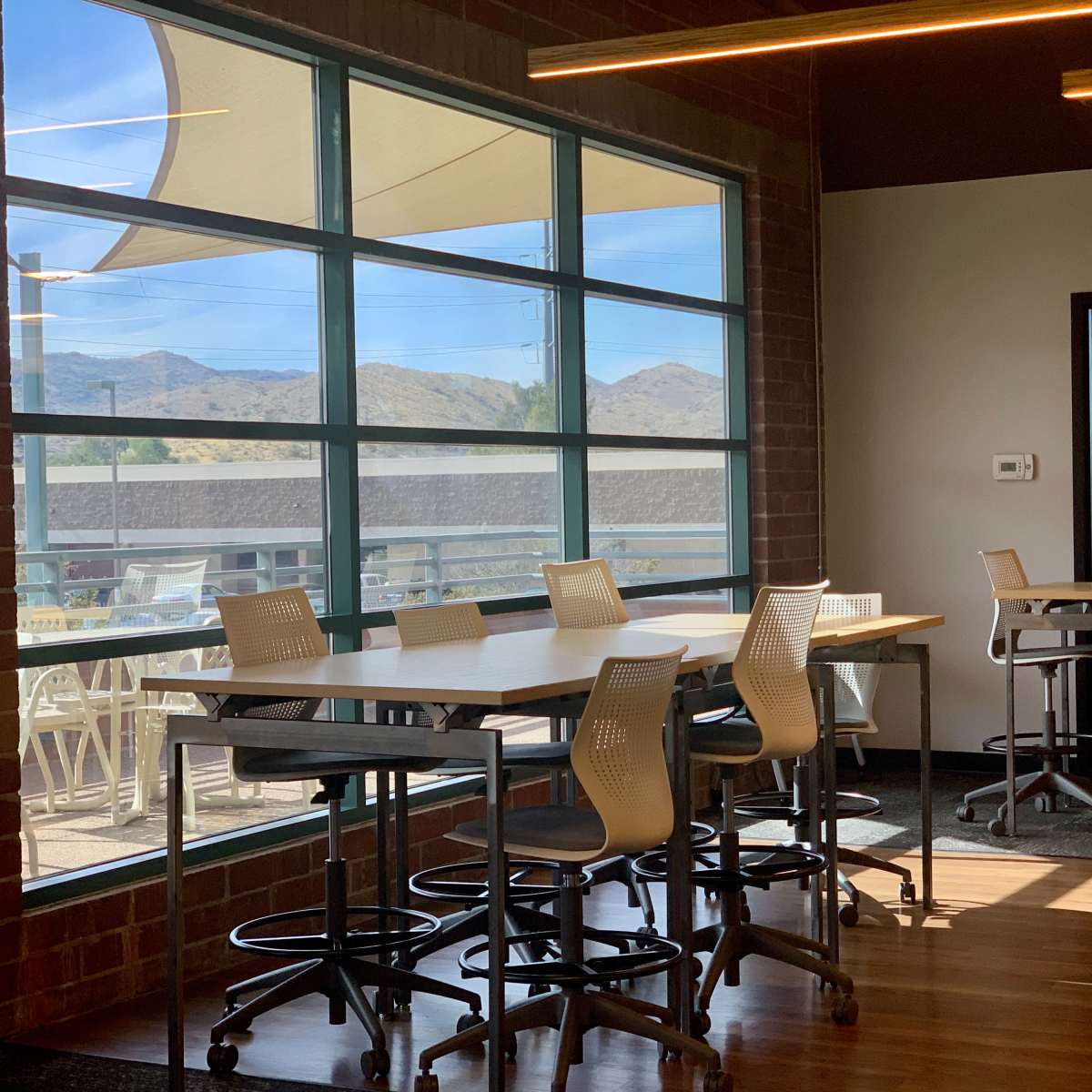 A well-lit interior space with tall windows, modern tables, and chairs facing a mountainous landscape outside.
