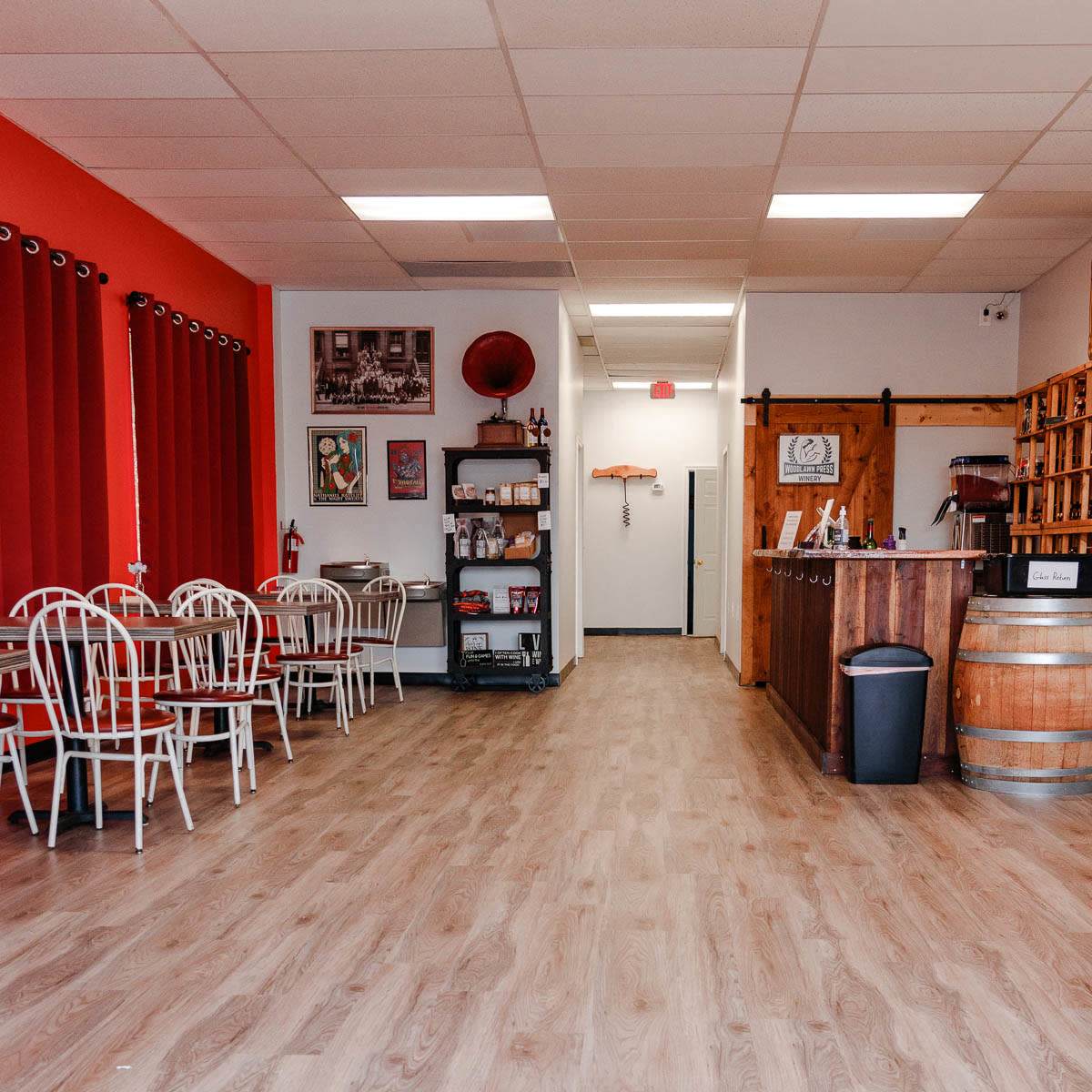 The interior of a restaurant features red walls, white metal chairs, a wooden counter, and a barrel, with a few decorative items on display.