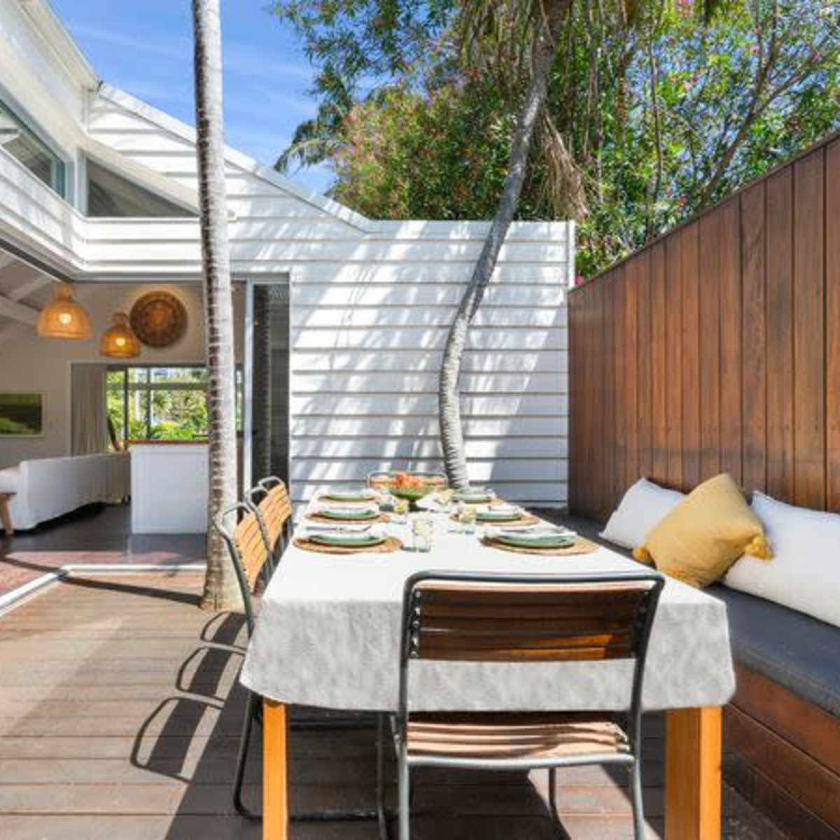 A spacious outdoor dining area is set with a table and chairs, surrounded by modern architecture and greenery.