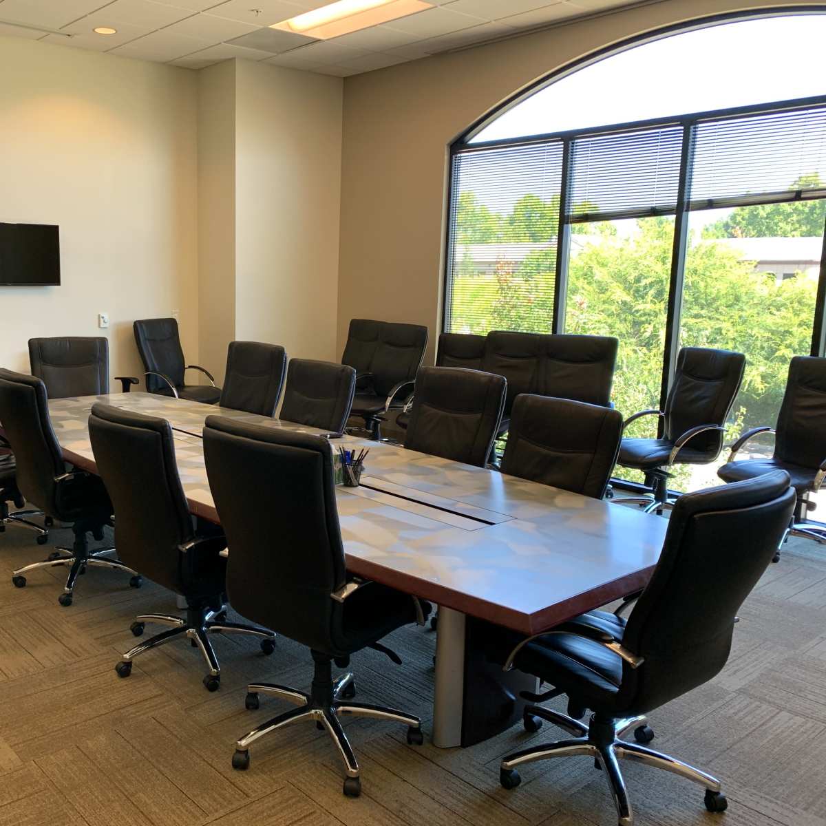 A large, modern conference room with a rectangular table surrounded by black ergonomic chairs, flanked by two wall-mounted screens.