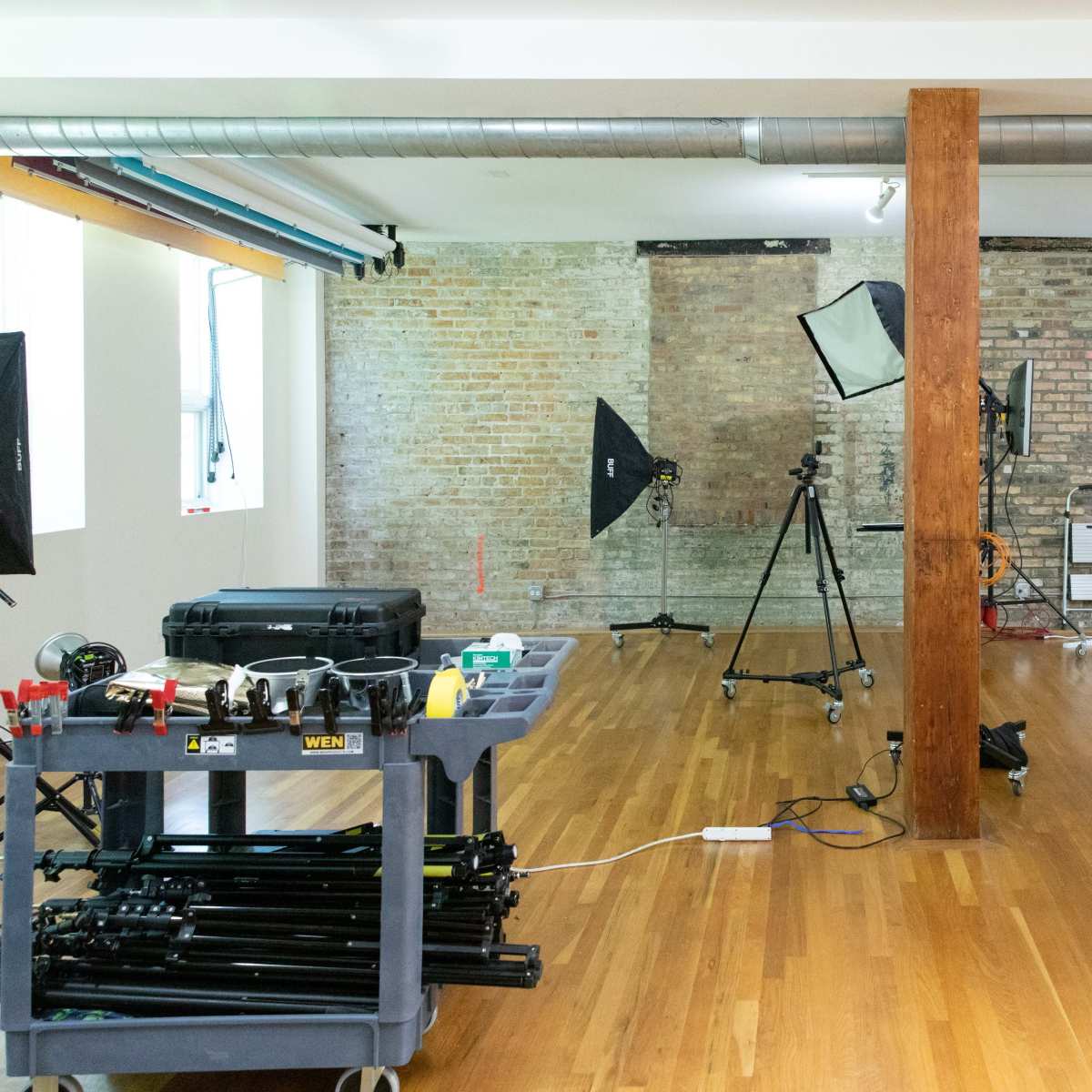 A spacious photography studio with equipment on wheels, a wooden beam, and a dog standing near the back wall.