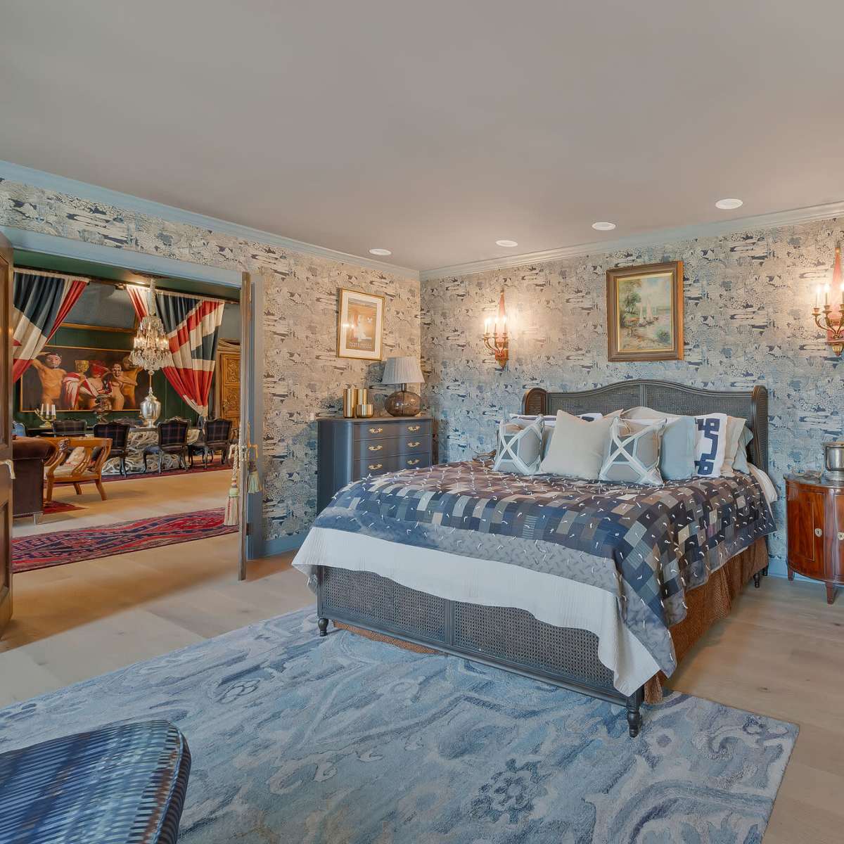 A bedroom featuring a bed with a patterned quilt, flanked by wall sconces, and decorated with a textured wallpaper.
