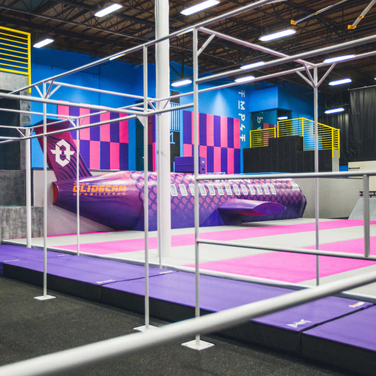 A colorful indoor trampoline park featuring a large, stylized airplane structure surrounded by various colored mats.