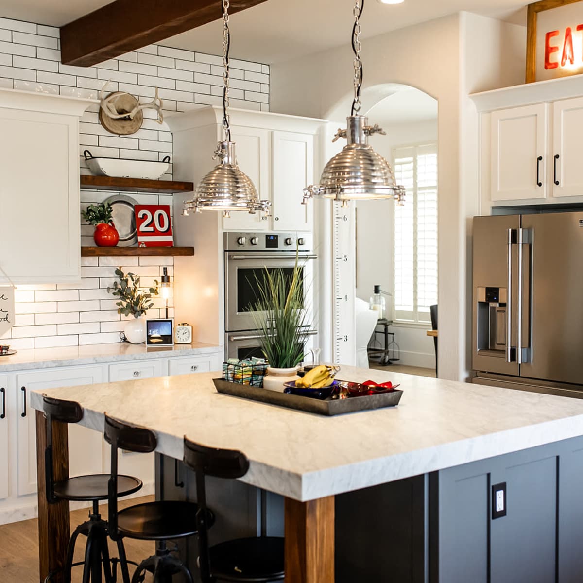 A modern kitchen with white cabinets, a large island featuring a marble countertop, and industrial-style pendant lights hanging above.