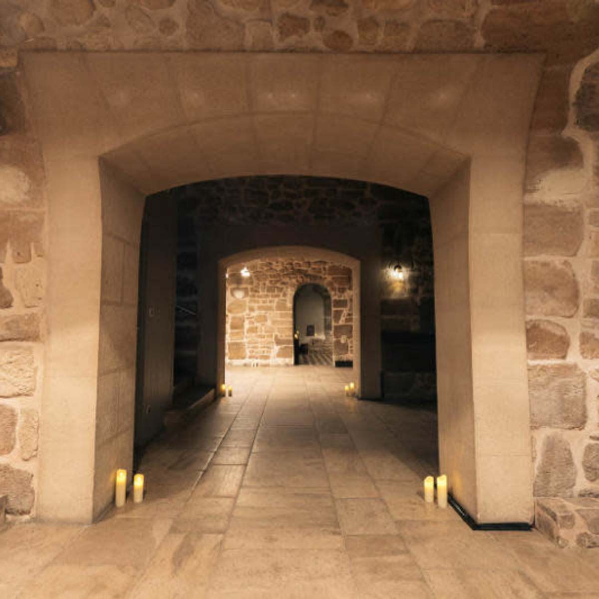 A stone-walled interior space with multiple archways and candles lining the floor.