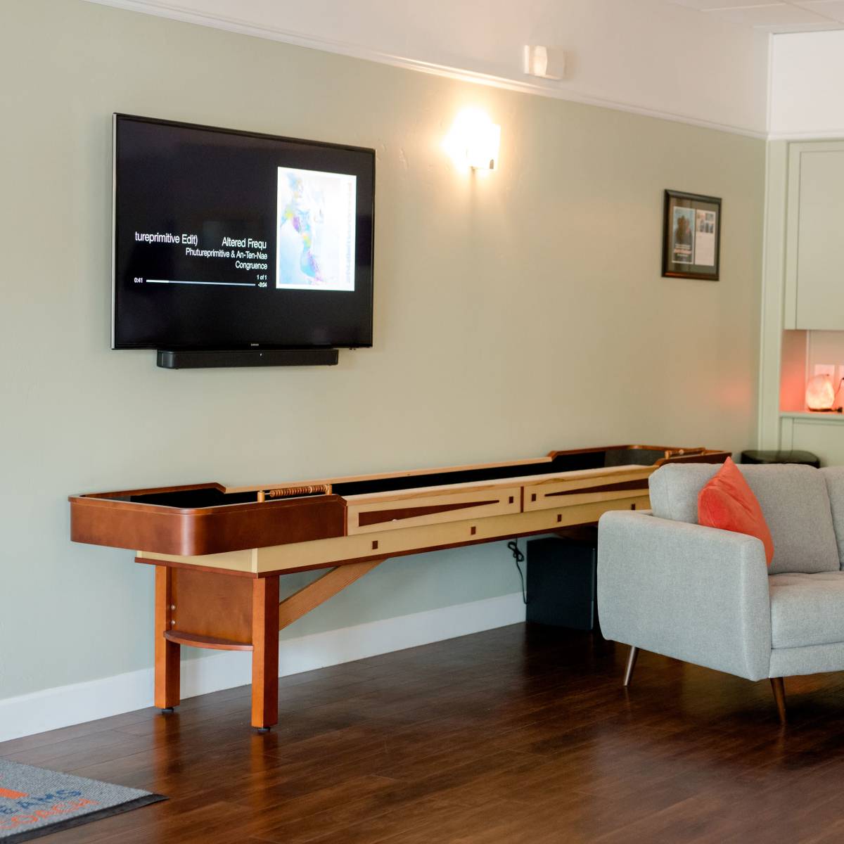 A modern living space with a gray sofa, a long wooden console underneath a television, and a small table in the background.