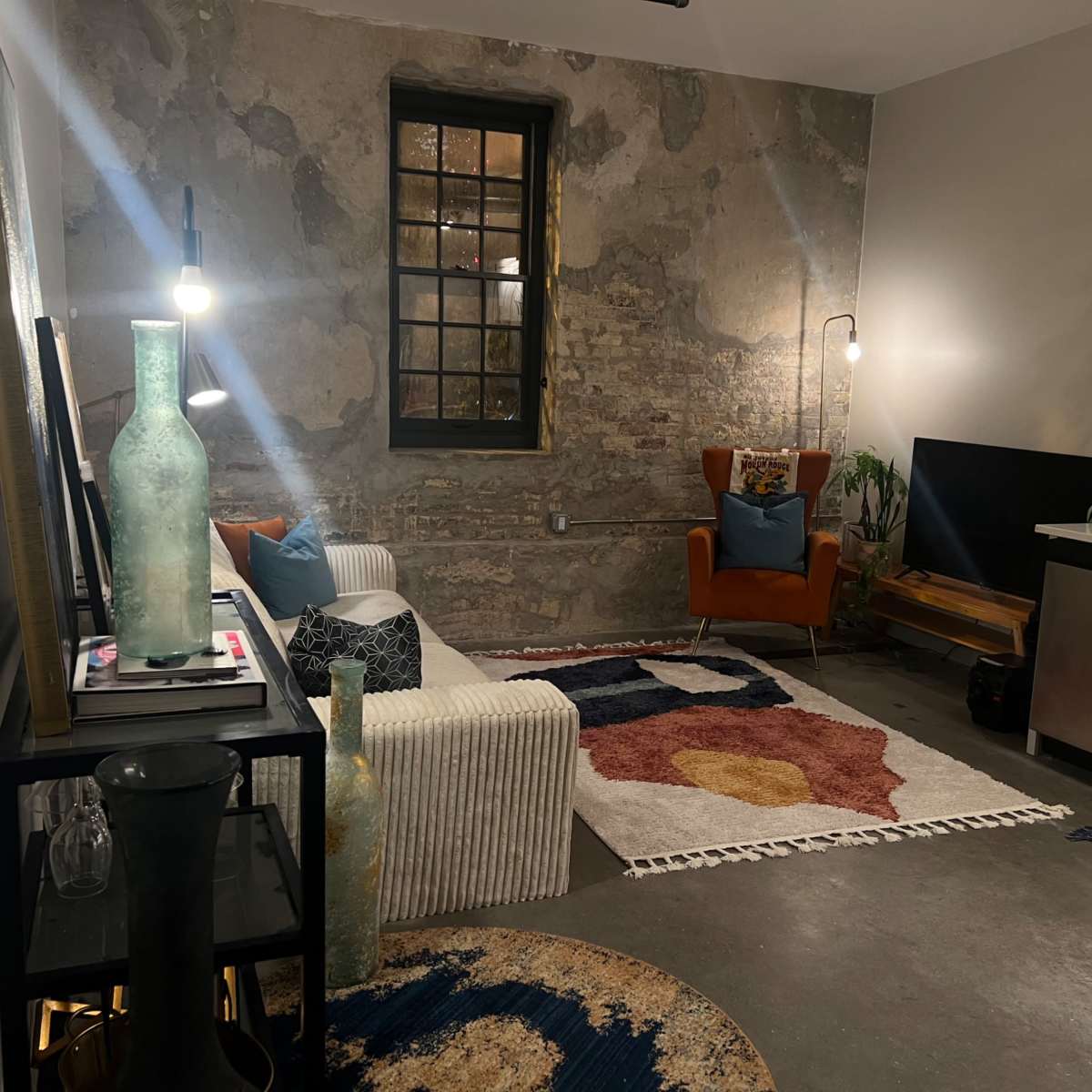A cozy living space with exposed brick walls, a colorful area rug, and a mix of modern and vintage furnishings.