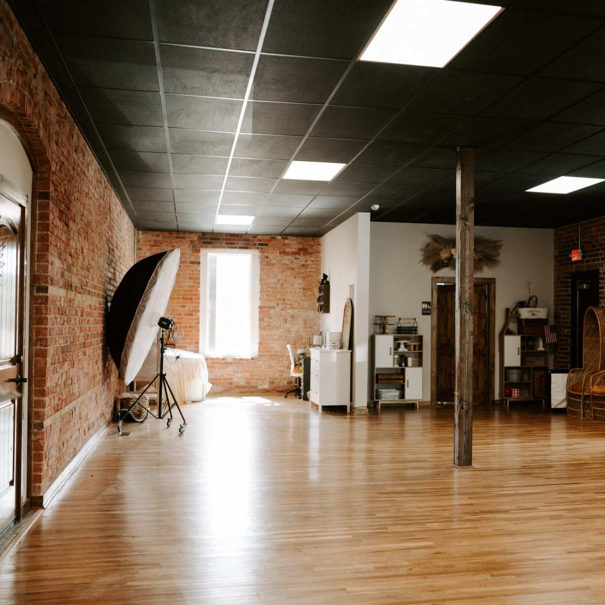 A spacious room with wooden flooring, exposed brick walls, and several clothing racks lined with garments.