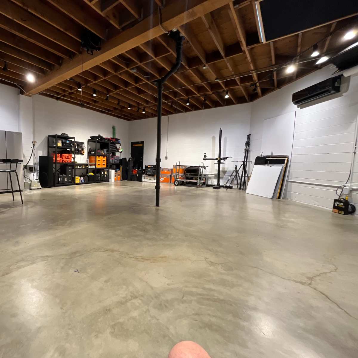 A spacious workshop with concrete flooring, various tools and equipment organized along the walls, and a table set up in the foreground.