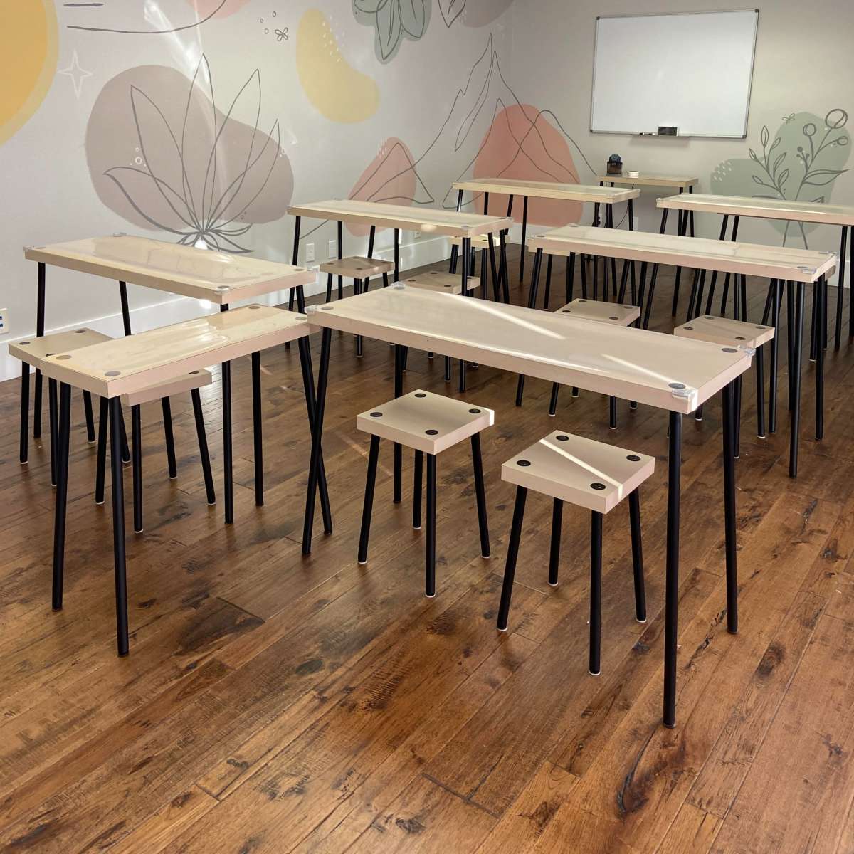 A group of wooden tables with black legs is arranged in a brightly lit room featuring a mural of plants and mountains on the wall.
