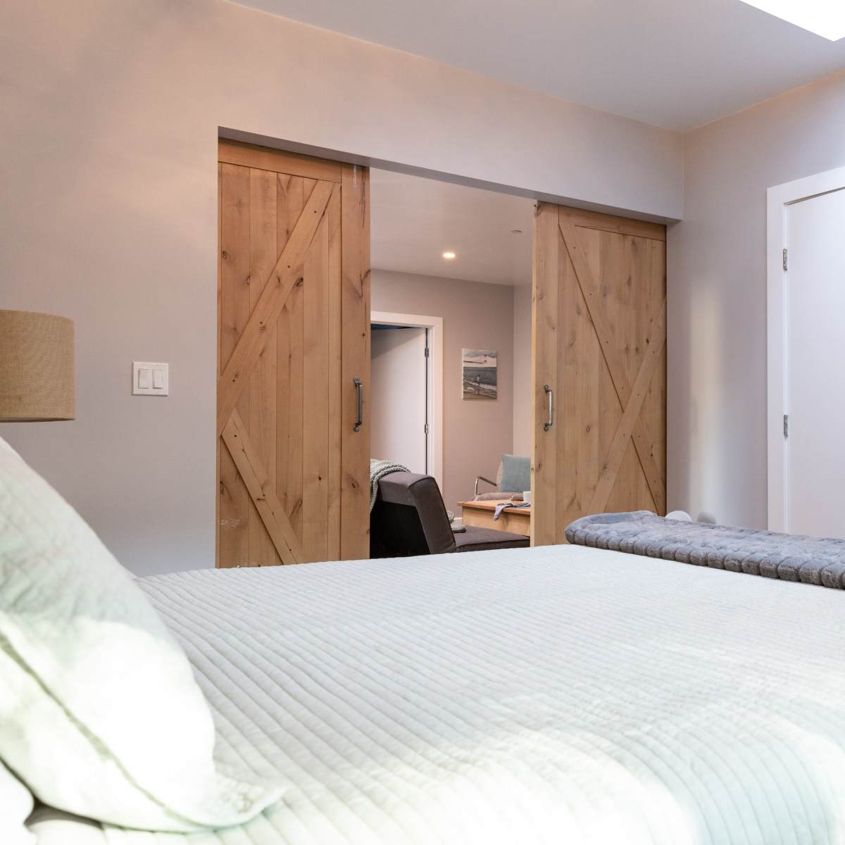 A softly lit bedroom with a bed in the foreground and wooden sliding doors leading to another room in the background.