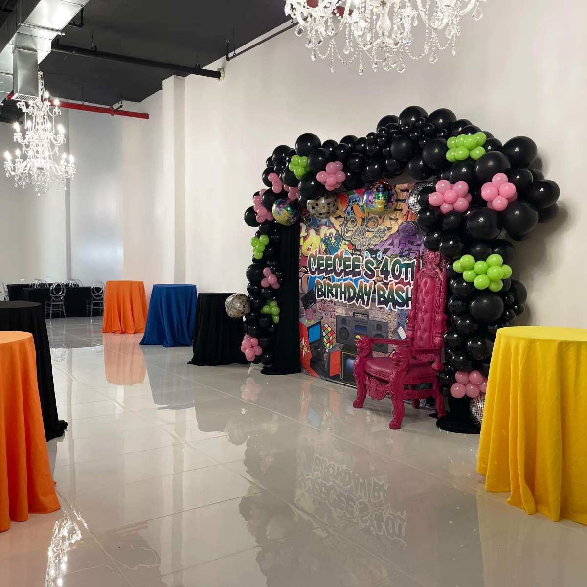 A brightly decorated event space featuring colorful tables and a large balloon arch with a birthday theme.