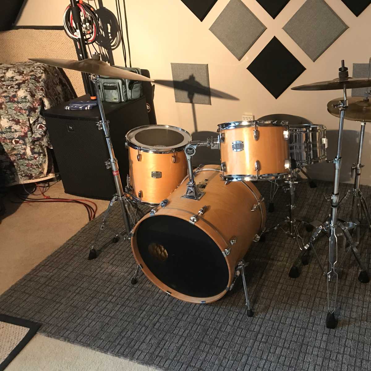 A wooden drum set with a bass drum, snare drum, and cymbals, positioned on a gray area rug in a music room.