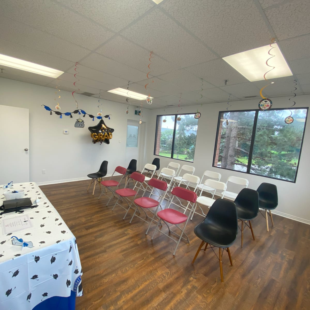 A decorated room with rows of chairs set up for a gathering, featuring a table with a festive tablecloth and graduation-themed decor hanging from the ceiling.