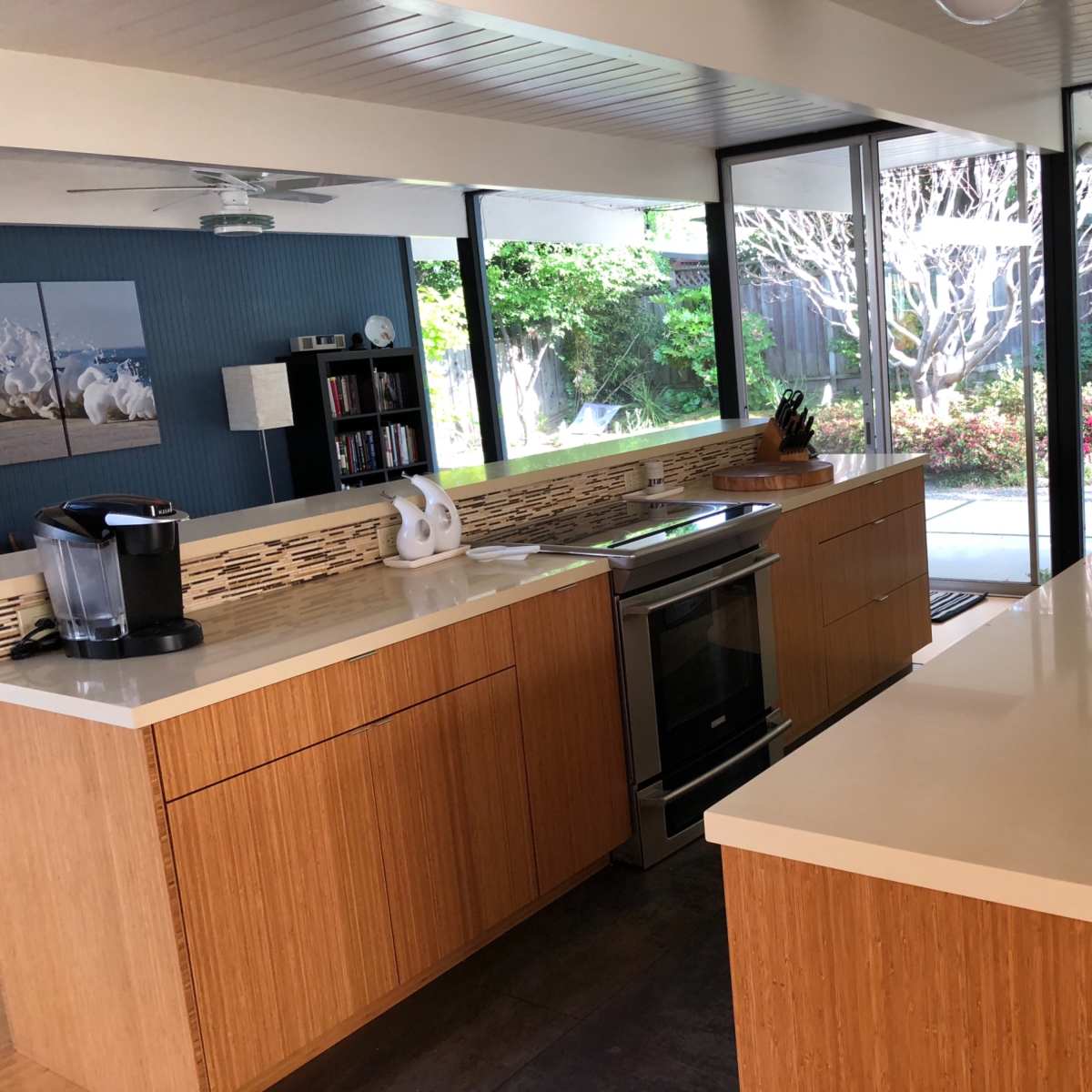 A modern kitchen with wooden cabinetry, a stainless steel oven, and large glass windows overlooking a landscaped garden.