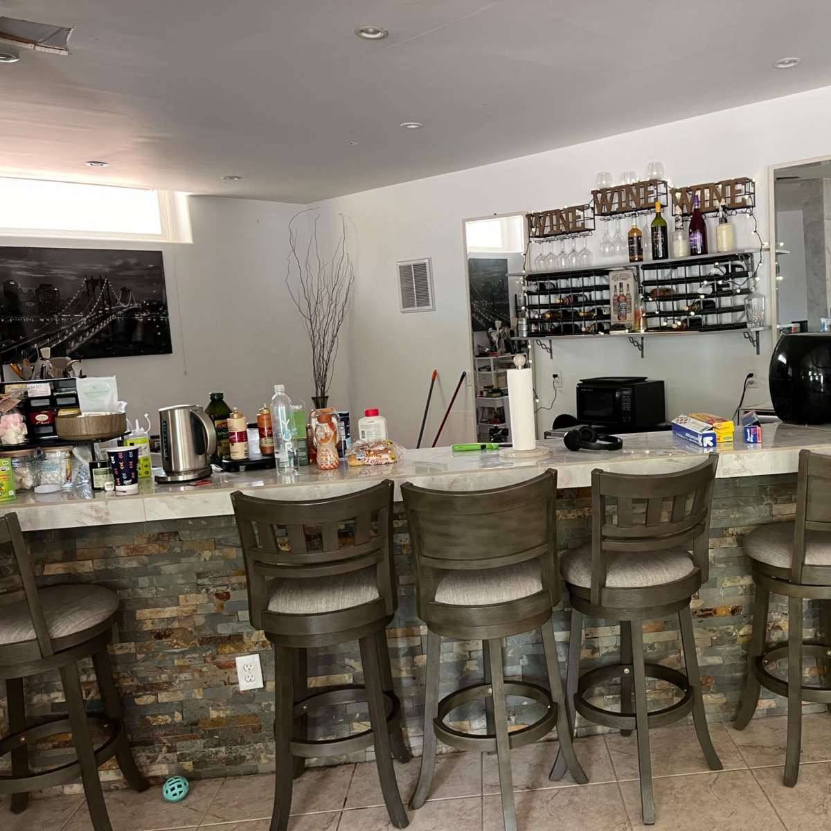 A modern kitchen bar area with eight stools, a counter decorated with various bottles and kitchen appliances, and a mirrored wall behind it.