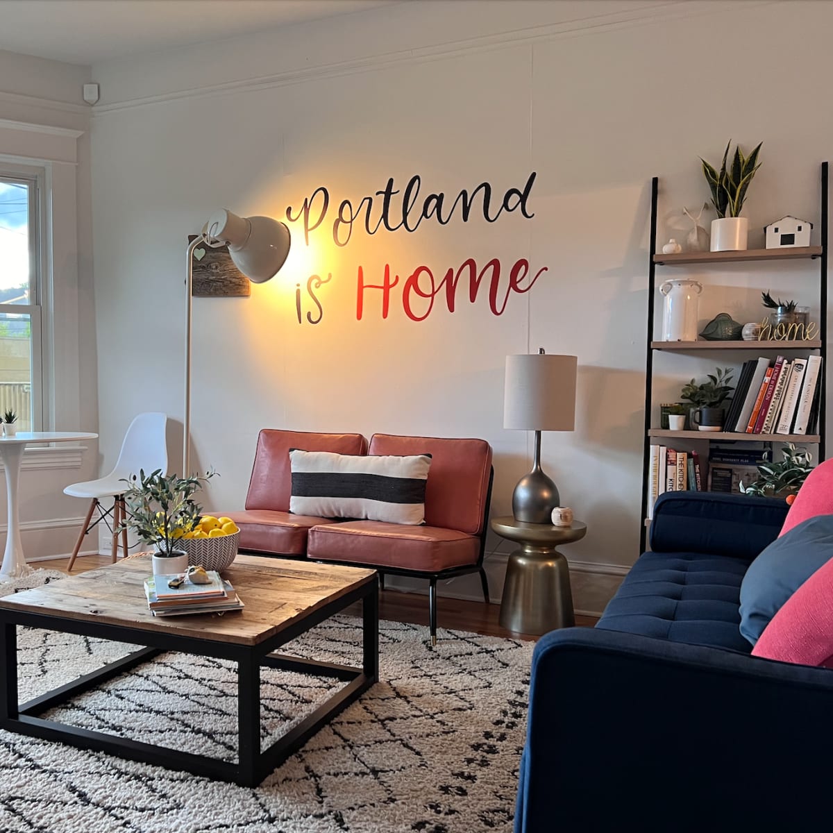 A stylish living room with a large coffee table, a pink couch, a blue couch, and a wall decorated with the phrase "Portland is Home."