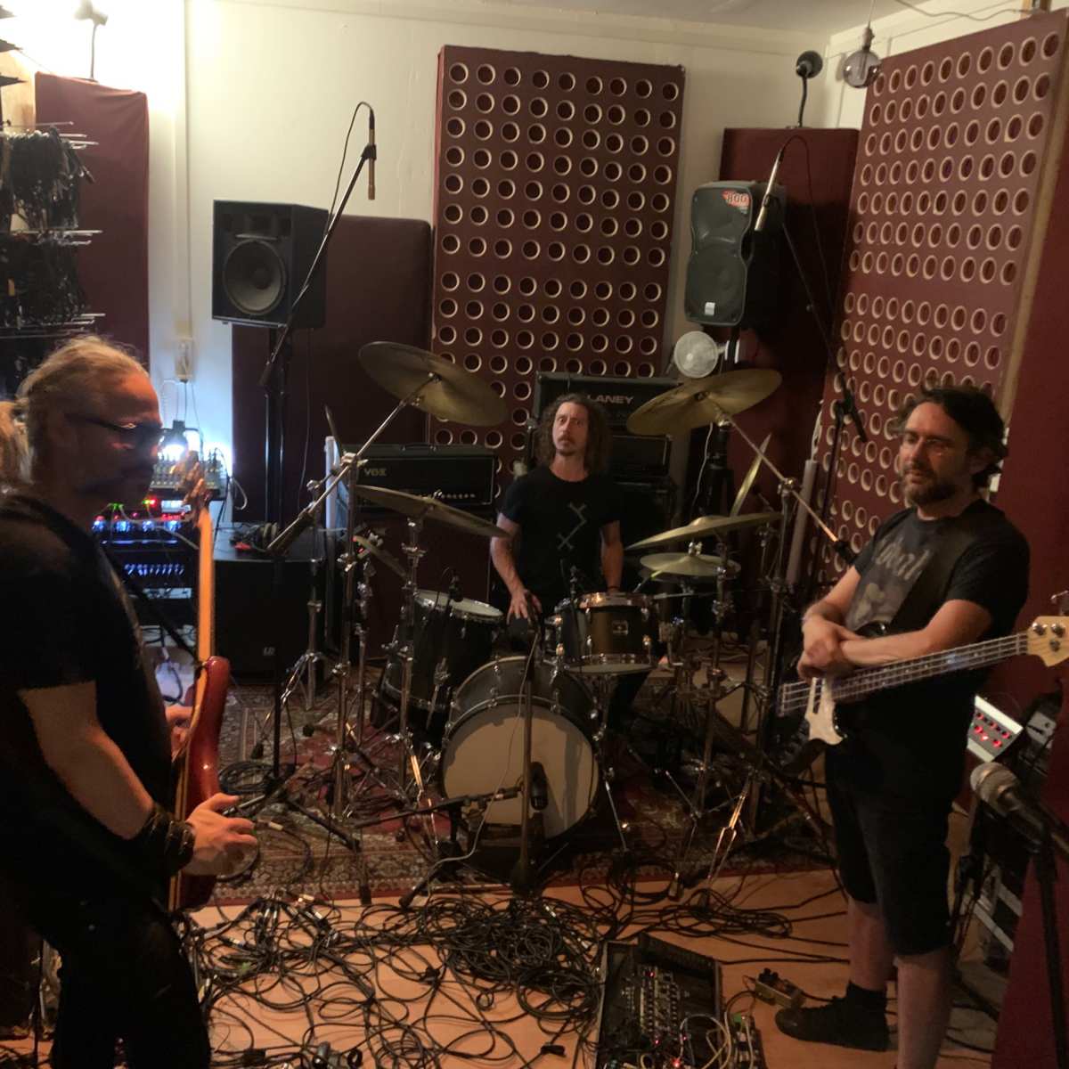 Three musicians are practicing in a soundproof room equipped with musical instruments and amplifiers.