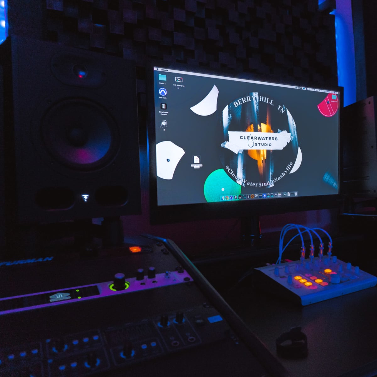 A music production studio setup featuring a computer monitor, mixer, and studio monitors amid colorful lighting.