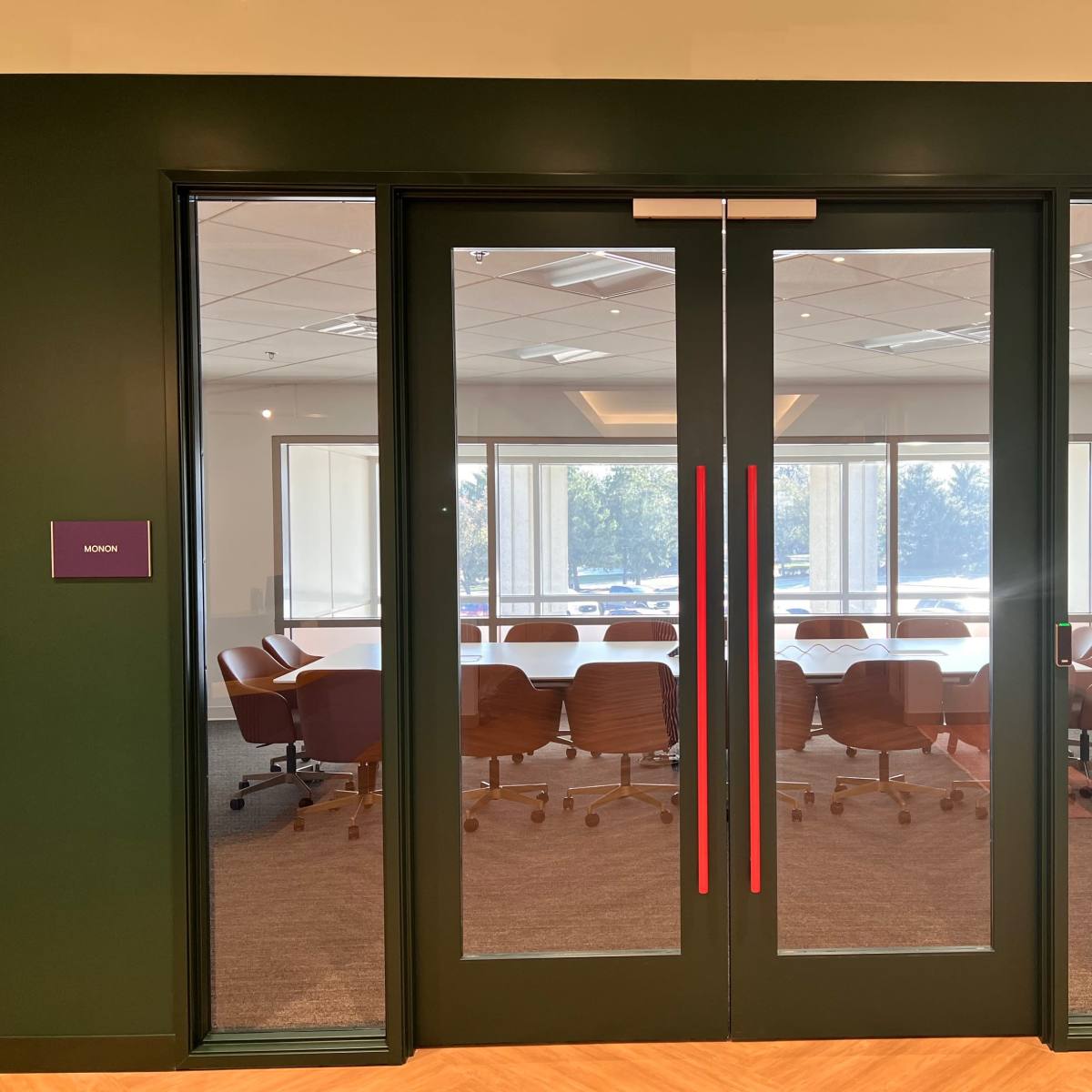 A glass double door leading to a conference room with brown chairs and a view of a well-lit, modern office space.