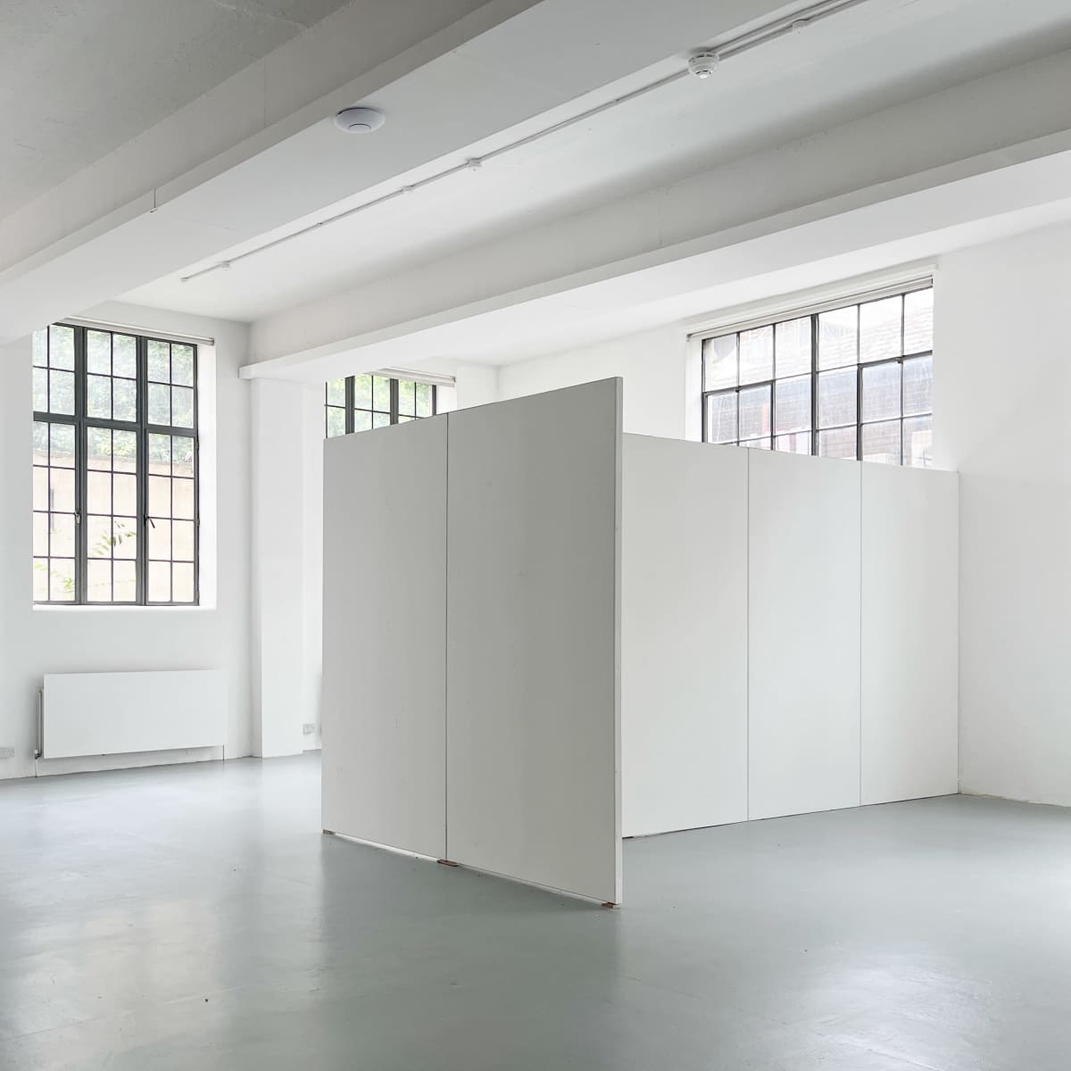 A spacious, minimalist room with white walls, large windows, and a partition dividing the space.