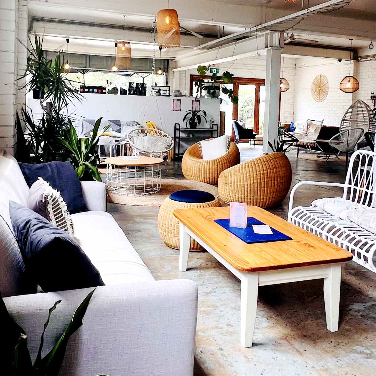 A modern indoor space featuring a white sofa, woven armchairs, a wooden coffee table, and various plants.