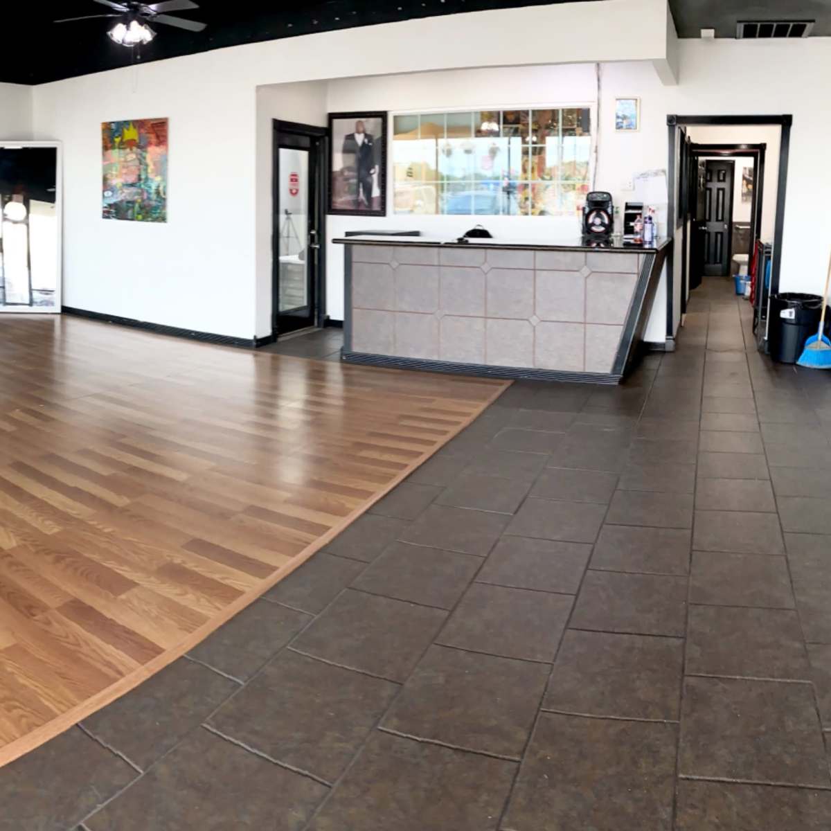 A spacious interior of a commercial space with wooden and tiled flooring, large windows, and a reception area.