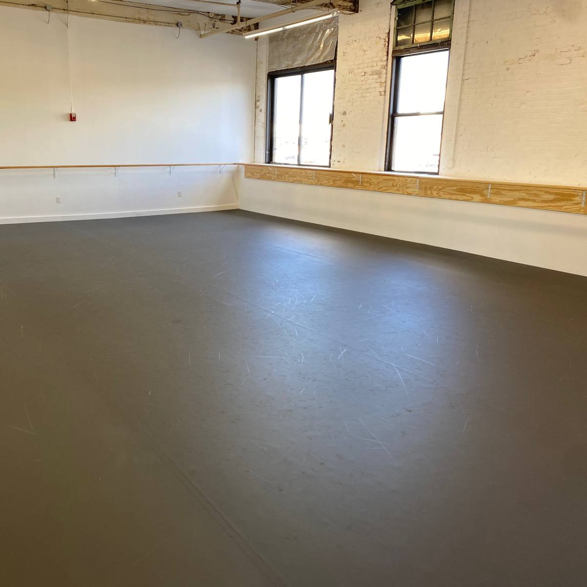 An empty dance studio with a smooth gray floor and large windows.