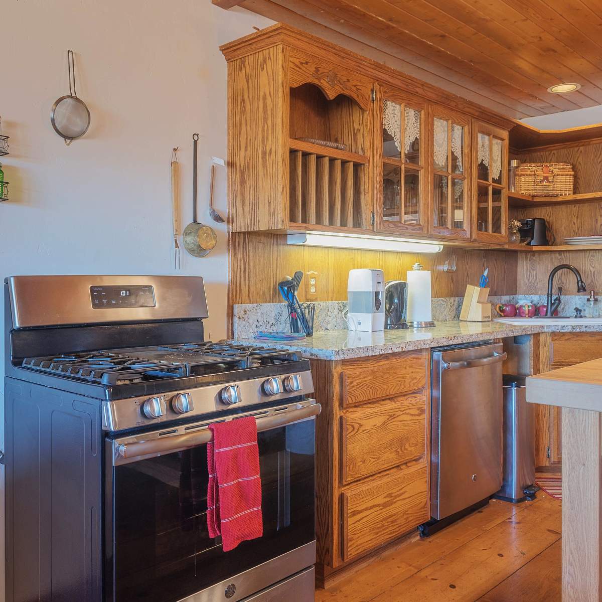 A kitchen with a stainless steel gas stove, wooden cabinets, a granite countertop, and a dishwasher next to a wooden island.