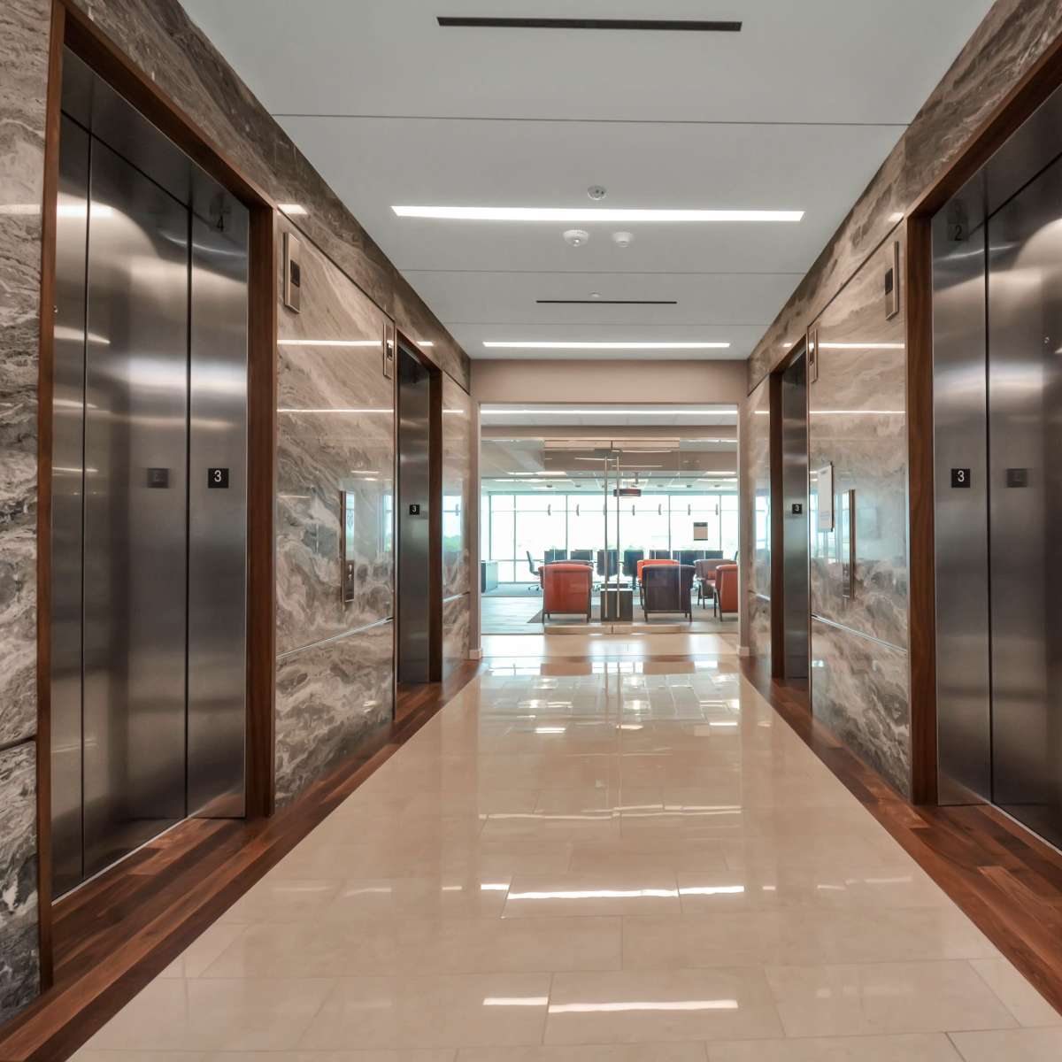 A spacious hallway featuring two sets of elevator doors on either side, with polished stone walls and a seating area visible at the end of the corridor.
