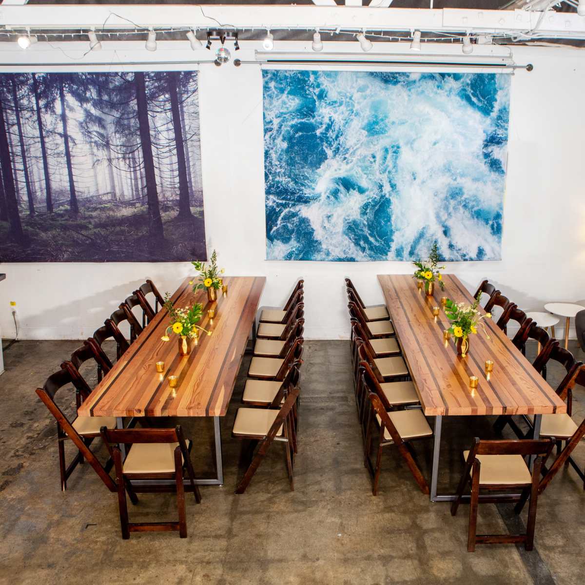 A spacious dining area features two large tables arranged in a U-shape, with floral centerpieces and artwork of a forest and ocean on the walls.