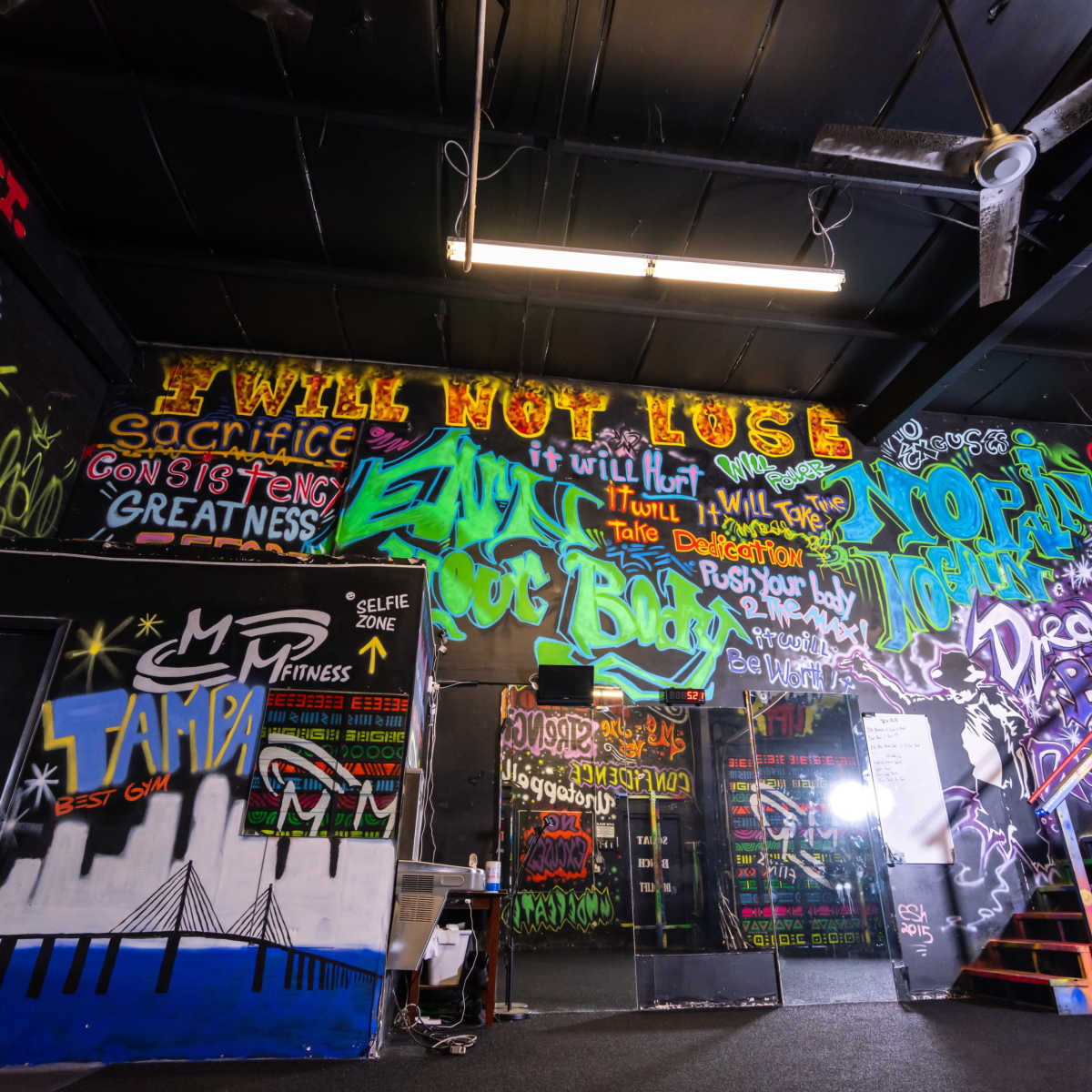 A gym interior featuring colorful graffiti on the walls with motivational phrases and artwork.