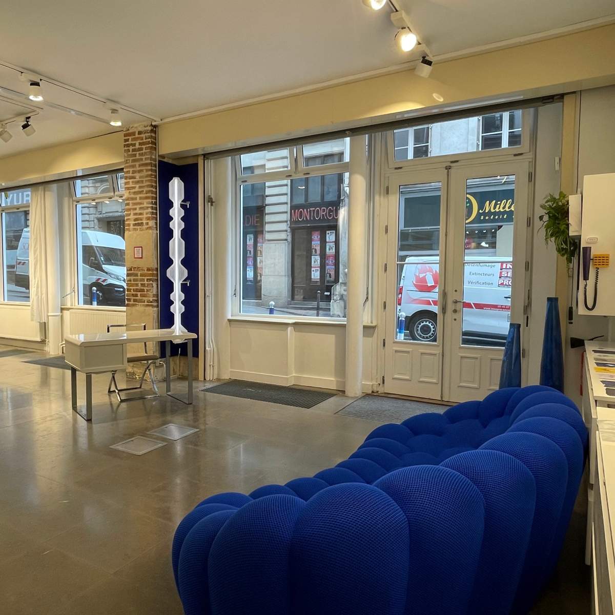 A modern interior space featuring a blue sofa, a small table, and large windows allowing natural light to enter.