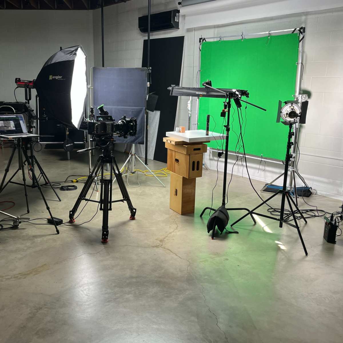 A video production studio setup with various cameras, lighting equipment, and a green screen in the background.