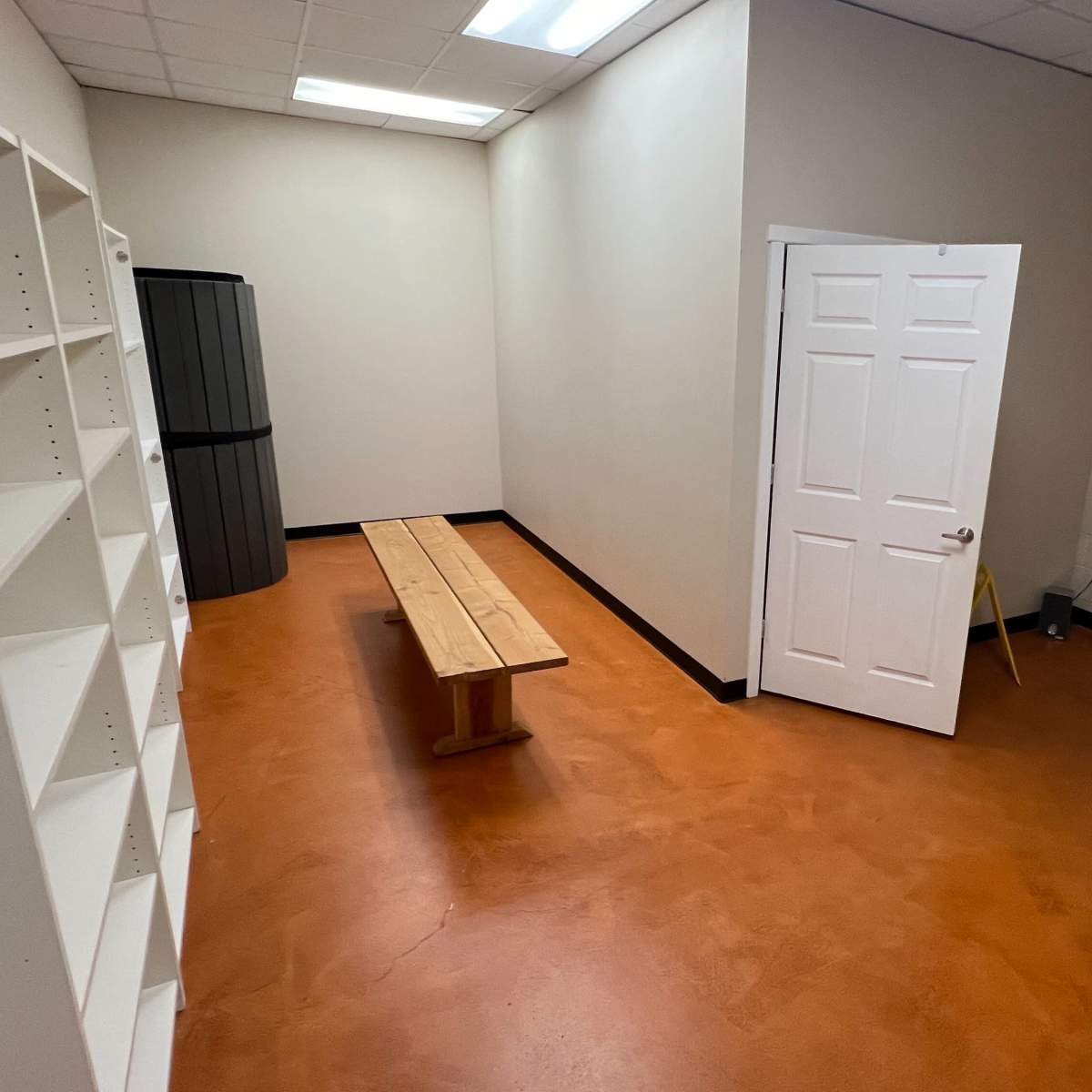 A small, empty room with a bench, shelf, and a door leading to another space.