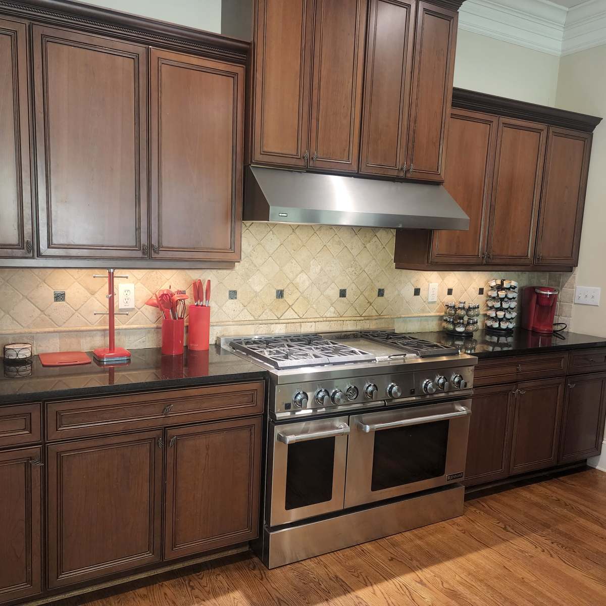 A spacious kitchen features dark wood cabinets, a stainless steel gas range, and a granite countertop with red and black accents.