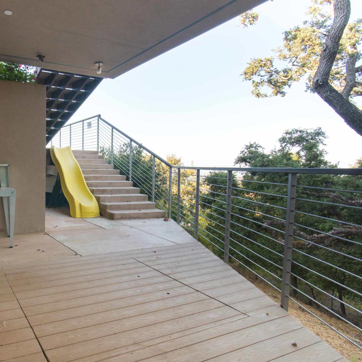 A patio area with a shower, a wooden bench, stairs leading up, and a yellow slide.