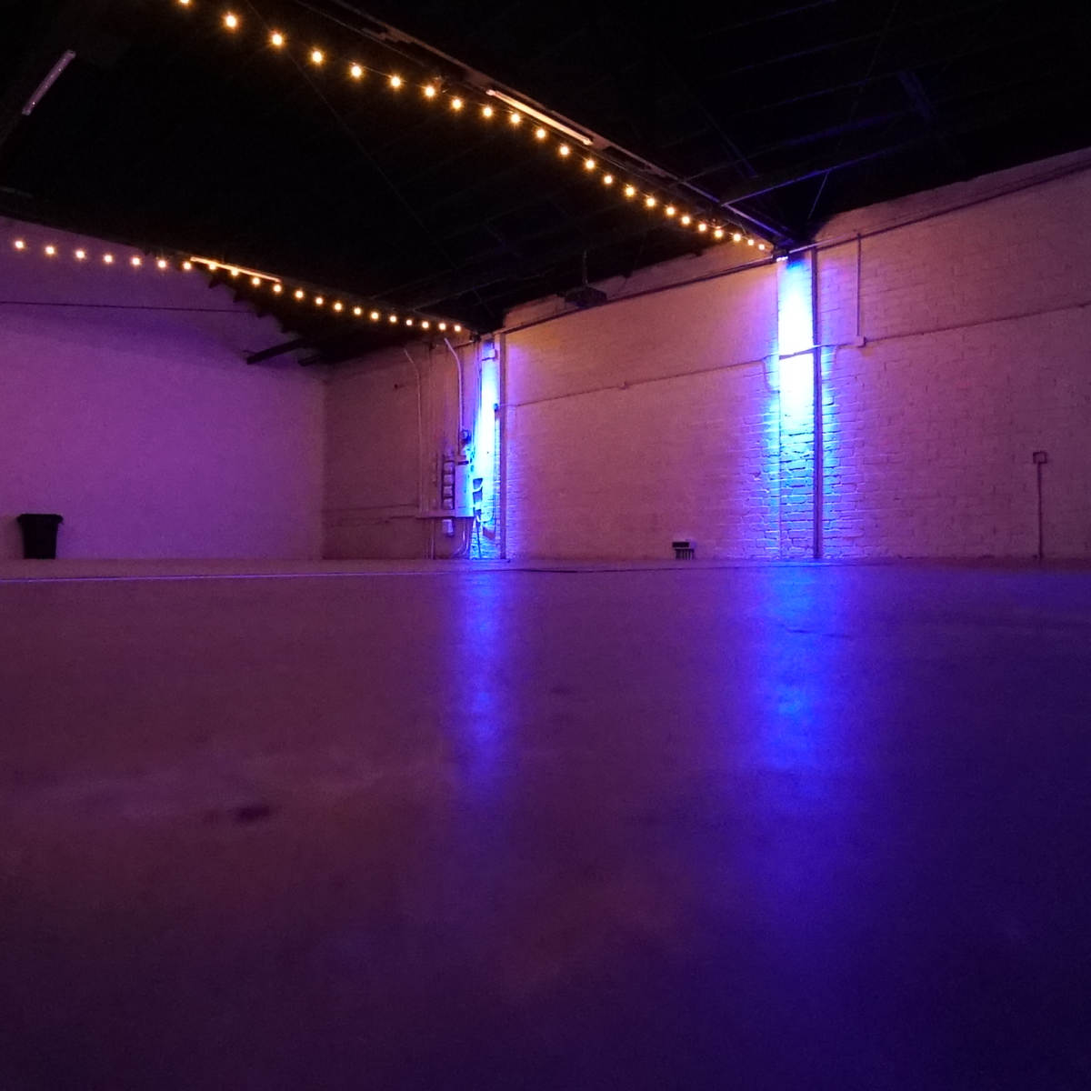 An empty, well-lit indoor space with a polished floor, exposed beams, and ambient lighting against the walls.