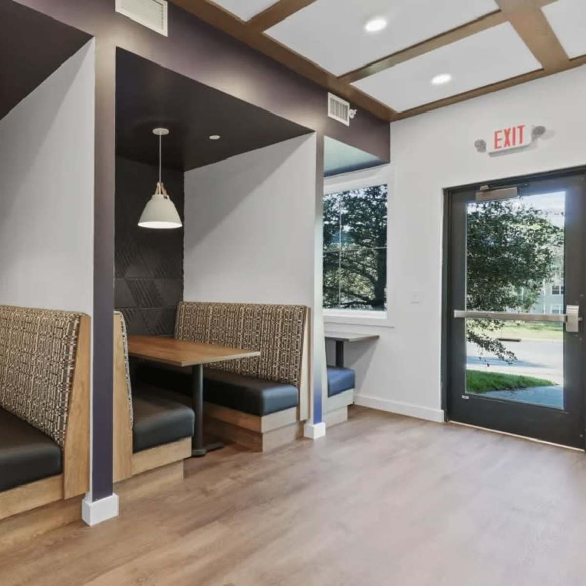 A modern cafe interior with two seating booths along the wall, featuring wooden tables and upholstered benches, alongside a door leading outside.