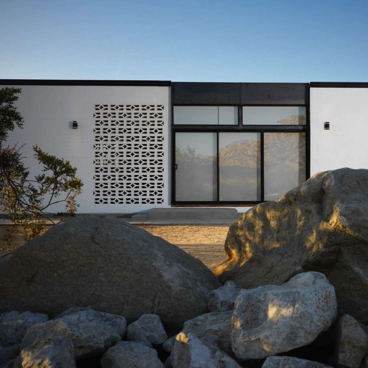 A modern building with large windows and a decorative wall panel stands in front of large boulders under a clear sky.