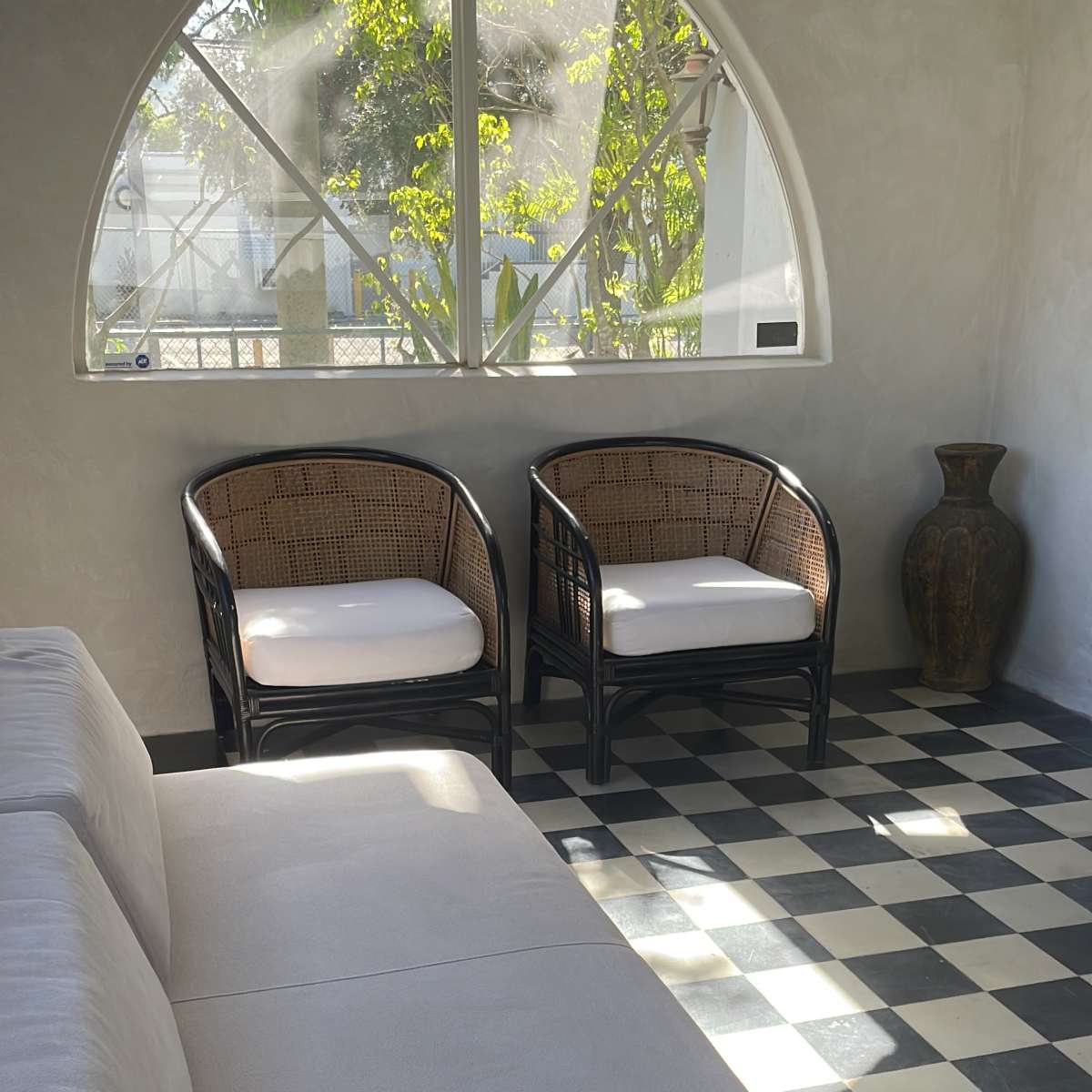 A minimalist interior with a low, light-colored sofa, two wicker chairs, and a decorative vase, all set against a black and white checkered floor.